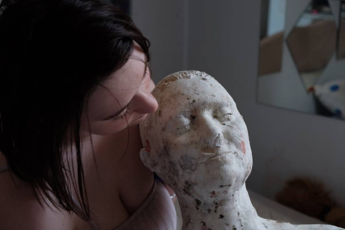A woman tenderly holding a plaster bust covered in bacteria and mold.