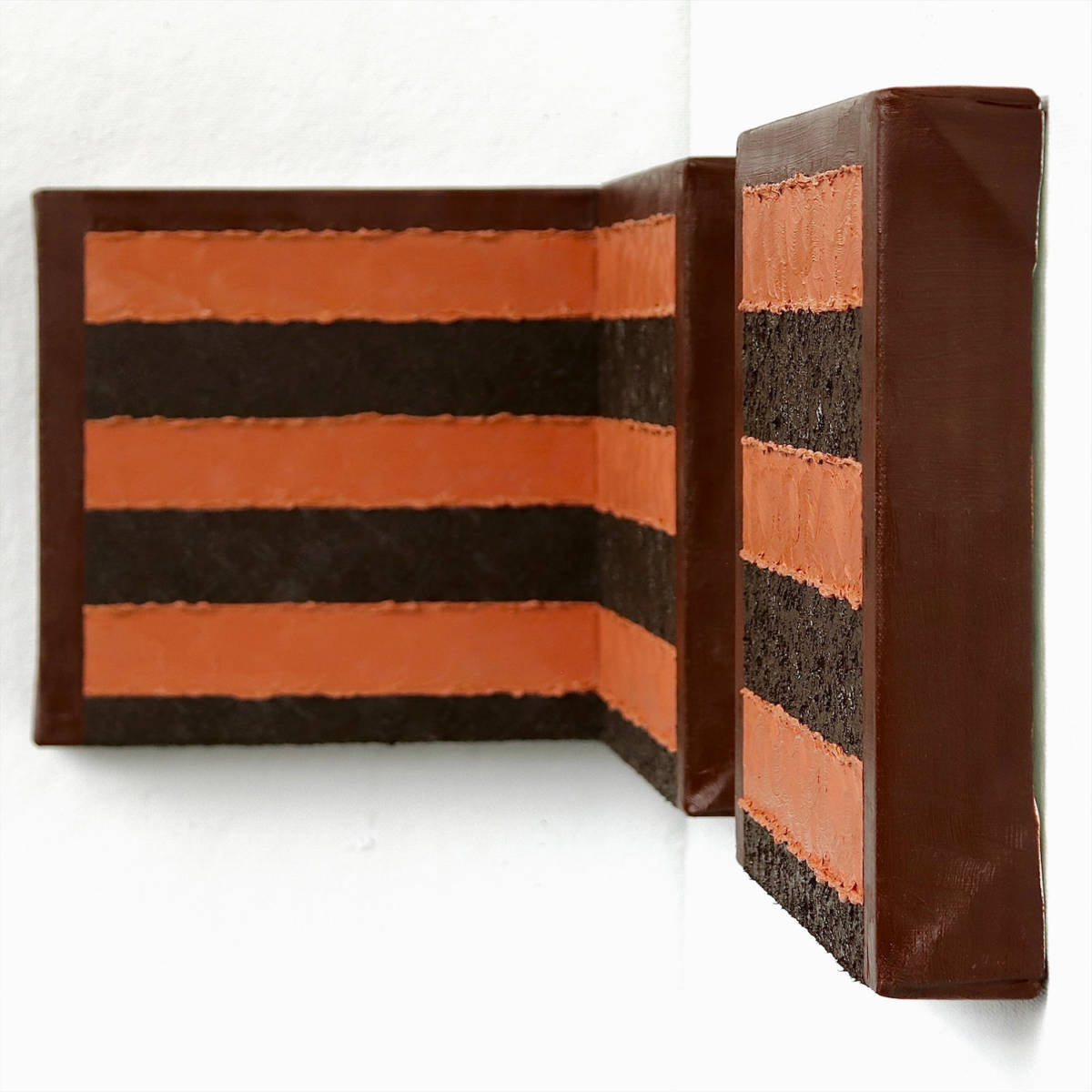 An impasto triptych of a chocolate cake that is installed in the corner