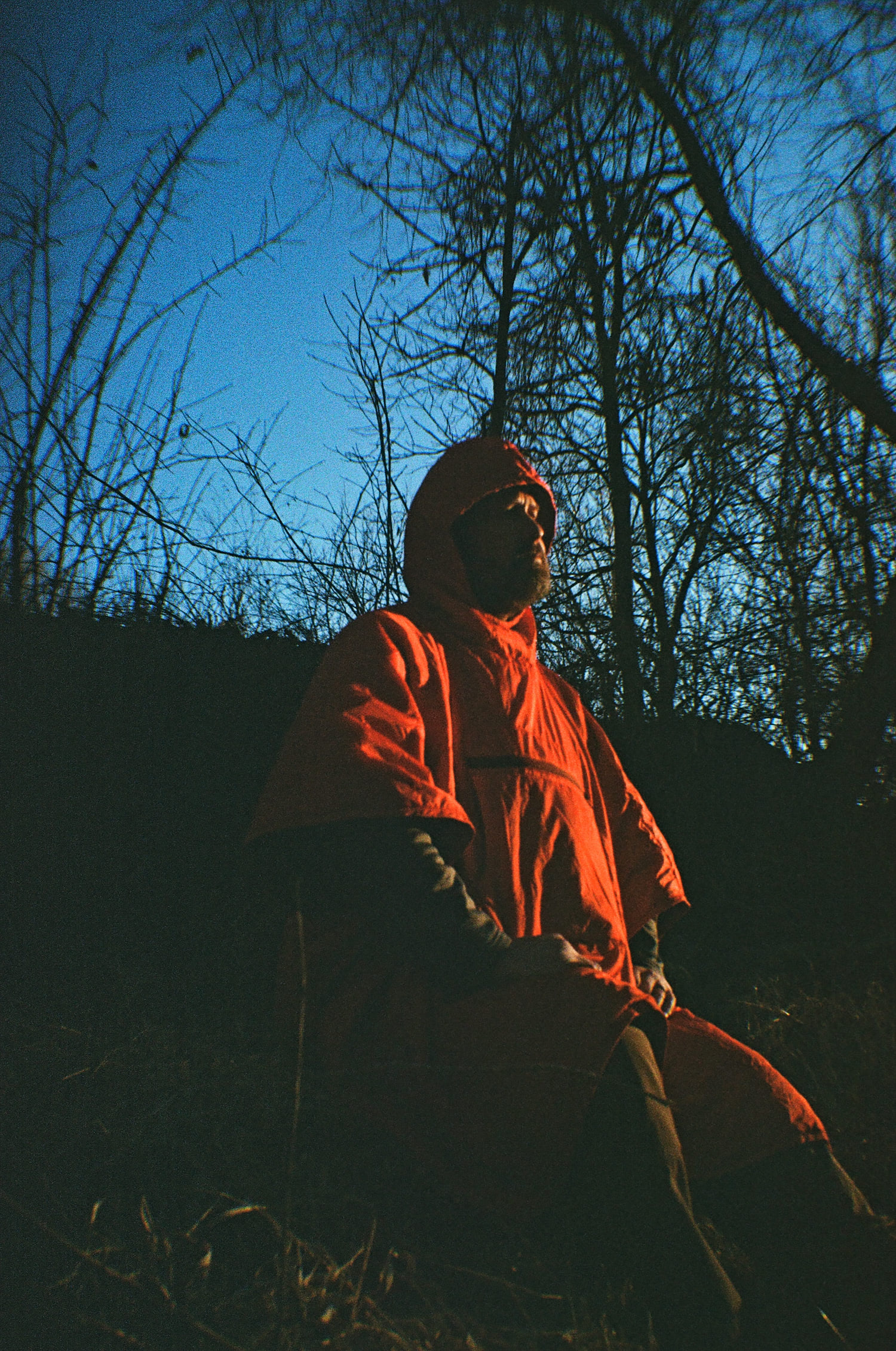 Sitting on a log, a man wearing an orange poncho absorbs the last of the day's sunshine.