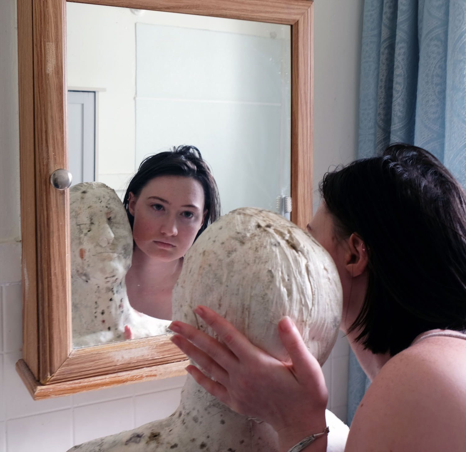 Photo of a woman and a plaster bust covered in bacteria reflected in a mirror.