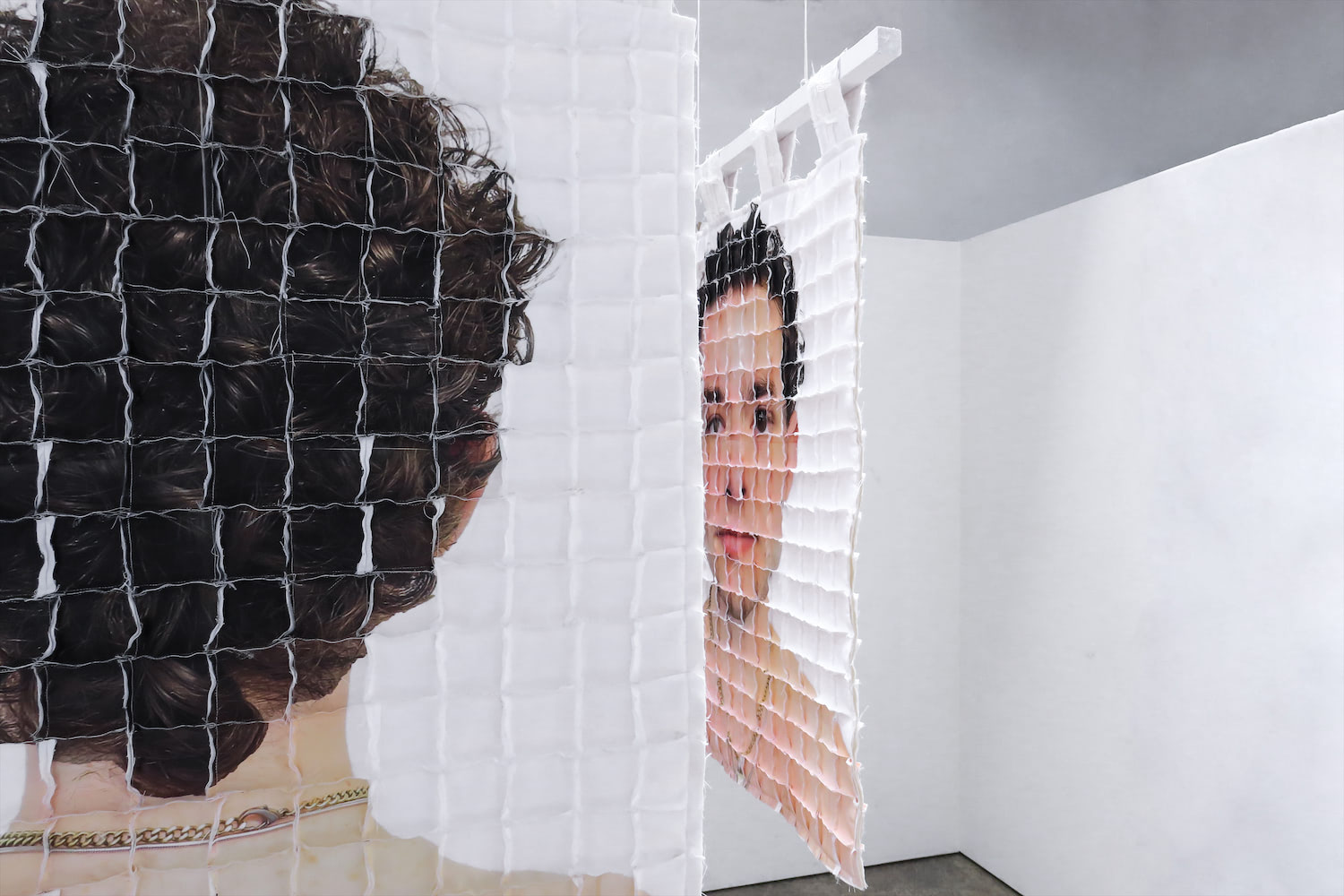 Two quilts are visible. On the left, half of one quilt faces towards the viewer, with the back of the artist's head visible.  On the right is the other quilt, showing the artist's face, distorted, at a severe angle.