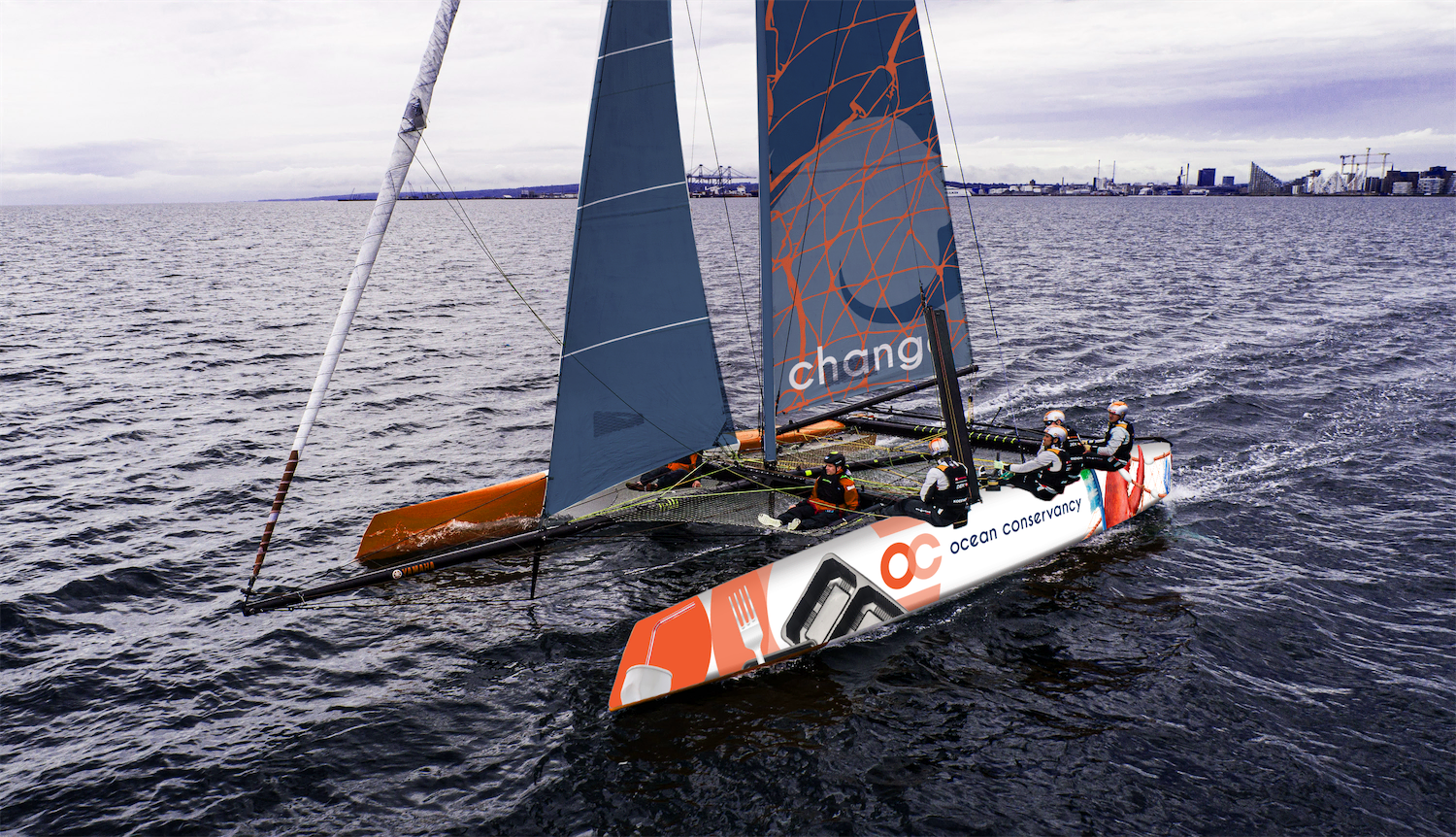 A GC32 racing sailboat mocked up to be sponsored by Ocean Conservancy. The blue sails have discarded orange fishing lines on them and the pontoons have trash amidst the logos to create the allusion that the boat is sailing through trash-filled harbors.