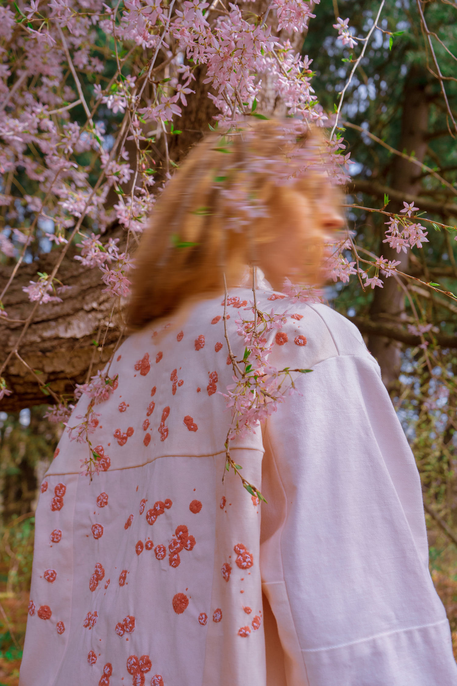 Model wearing Psoriasis jacket, facing back, looking over her shoulder, under a blossoming tree