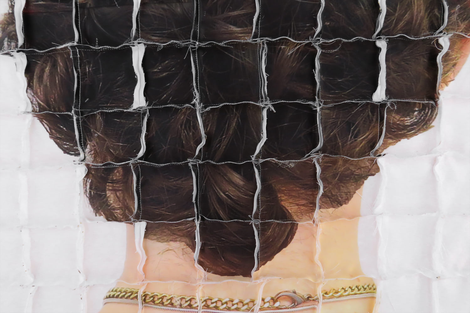 A detail shot of one of the quilts with the just the nape of the neck showing. The  close up of brown-haired curls and a gold chain is distorted by seams that form a grid pattern.