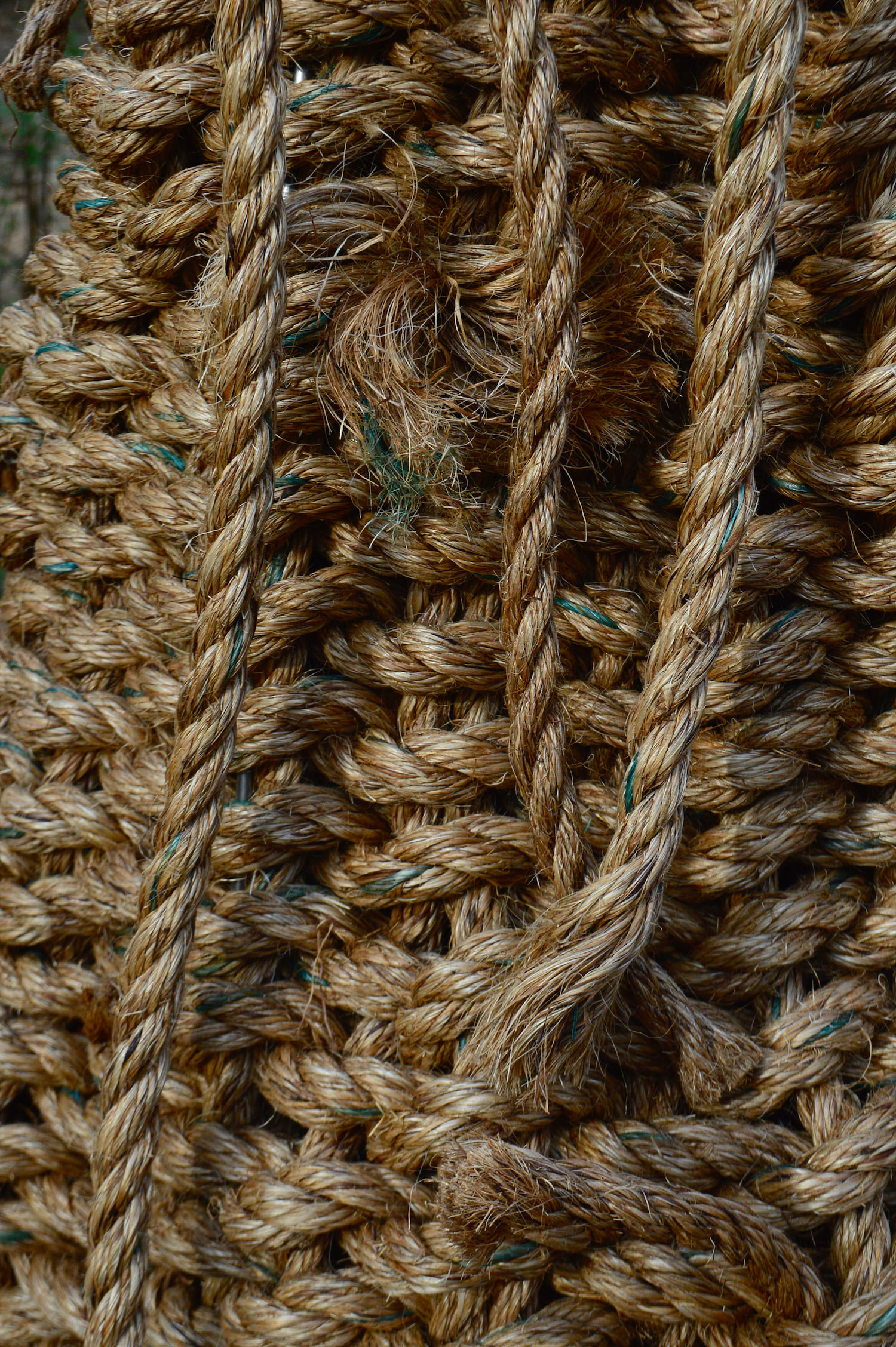 This detail shot captures the outer facade of the basket from mid-height. The directionality of the horizontal weavers, which are slightly angled upwards and to the right, are emphasized. One of the weavers, which is replaced by an additional rope segment, is untucked, resulting in the visibility of its protruding, frayed edge. Three hanging warps hug the surface of the sculpture. The two on the right hand-side cross near their edges.