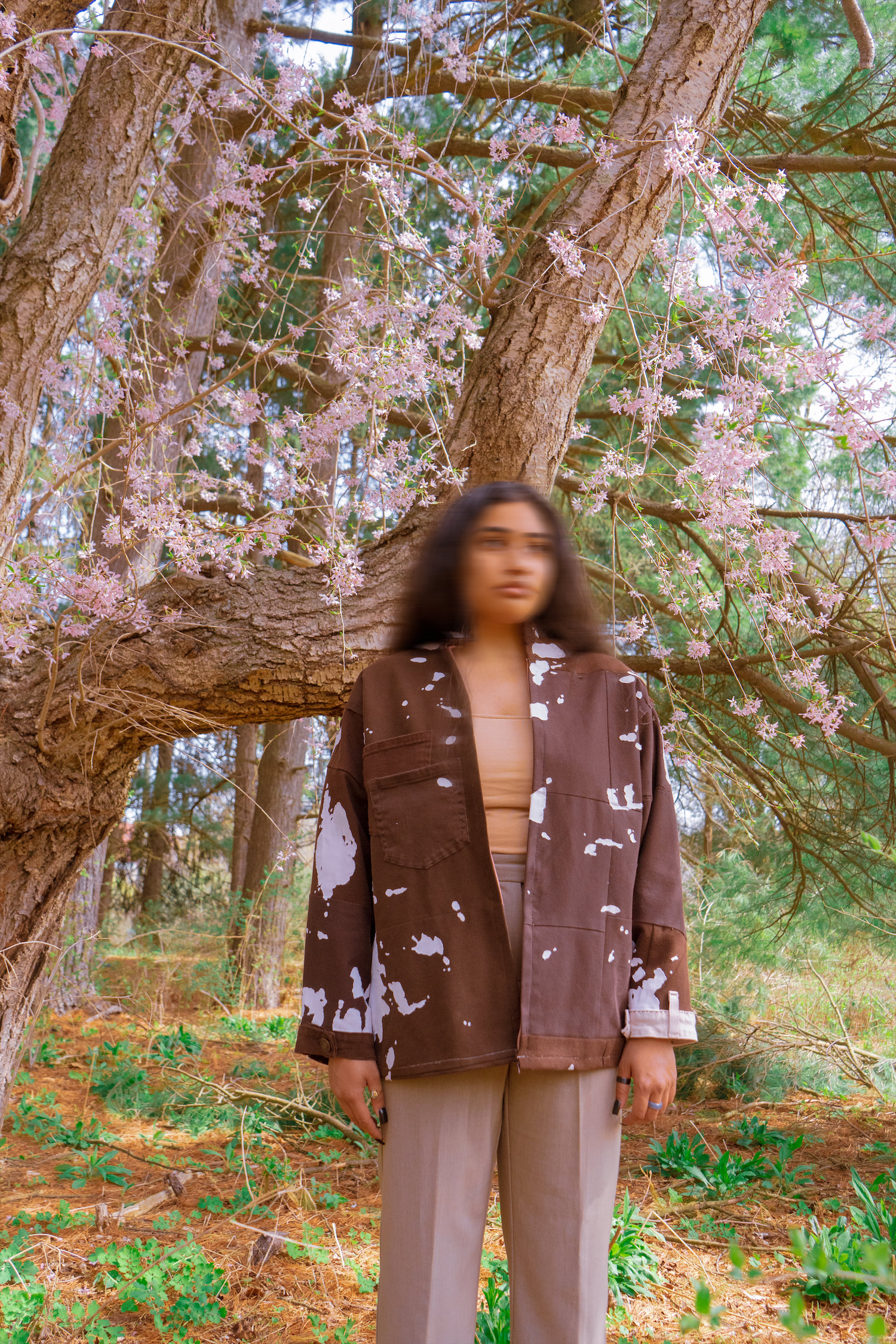 Model wearing Vitiligo jacket, facing forward, under a blossoming tree
