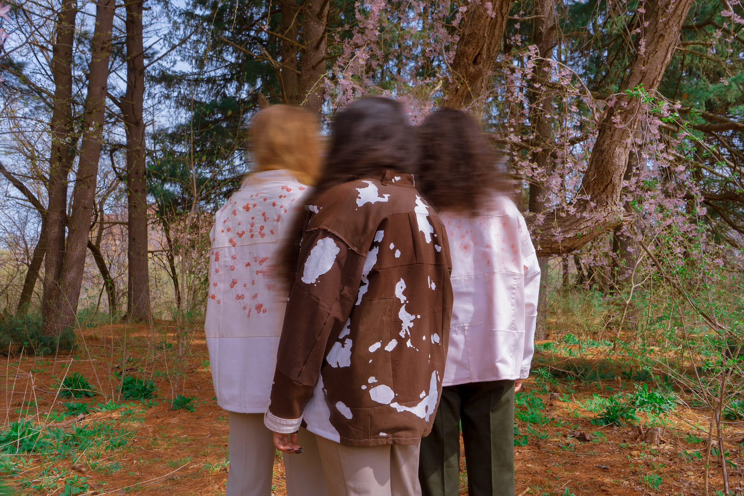 Three models wearing hand stitched jackets, all facing back with their heads blurred.