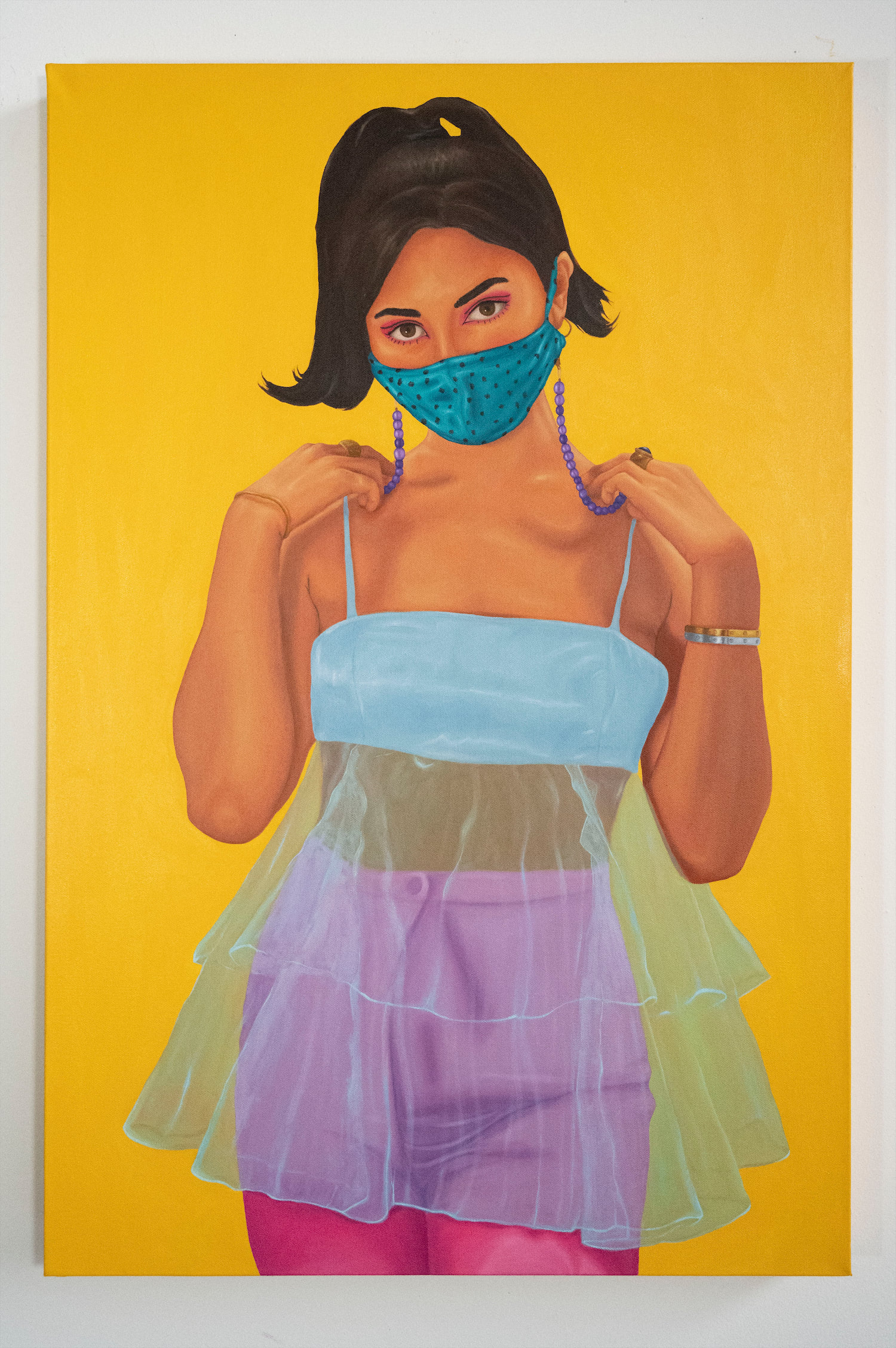 Megan wearing a light blue bra with tulle and pink leather pants, accessorized with an aqua polka dot mask and purple beaded chain with gold and silver jewelry.