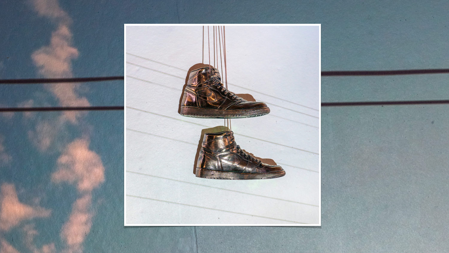 A pair of cast bronze Air Jordan sneakers hang in front of a projected sky and telephone wires.