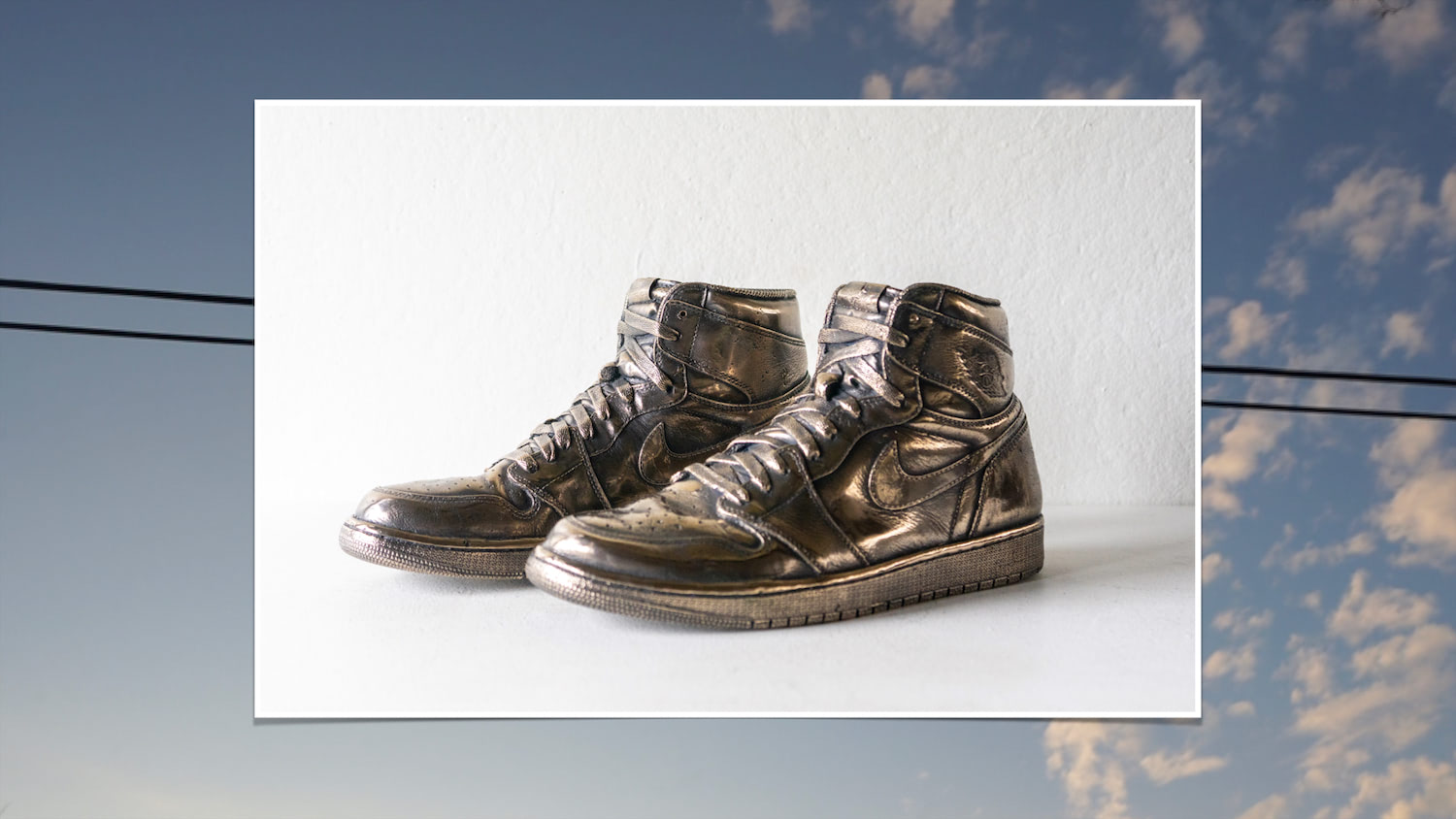 Air Jordan 1's cast in solid bronze, size 12 with blue sky, clouds, and telephone wire.