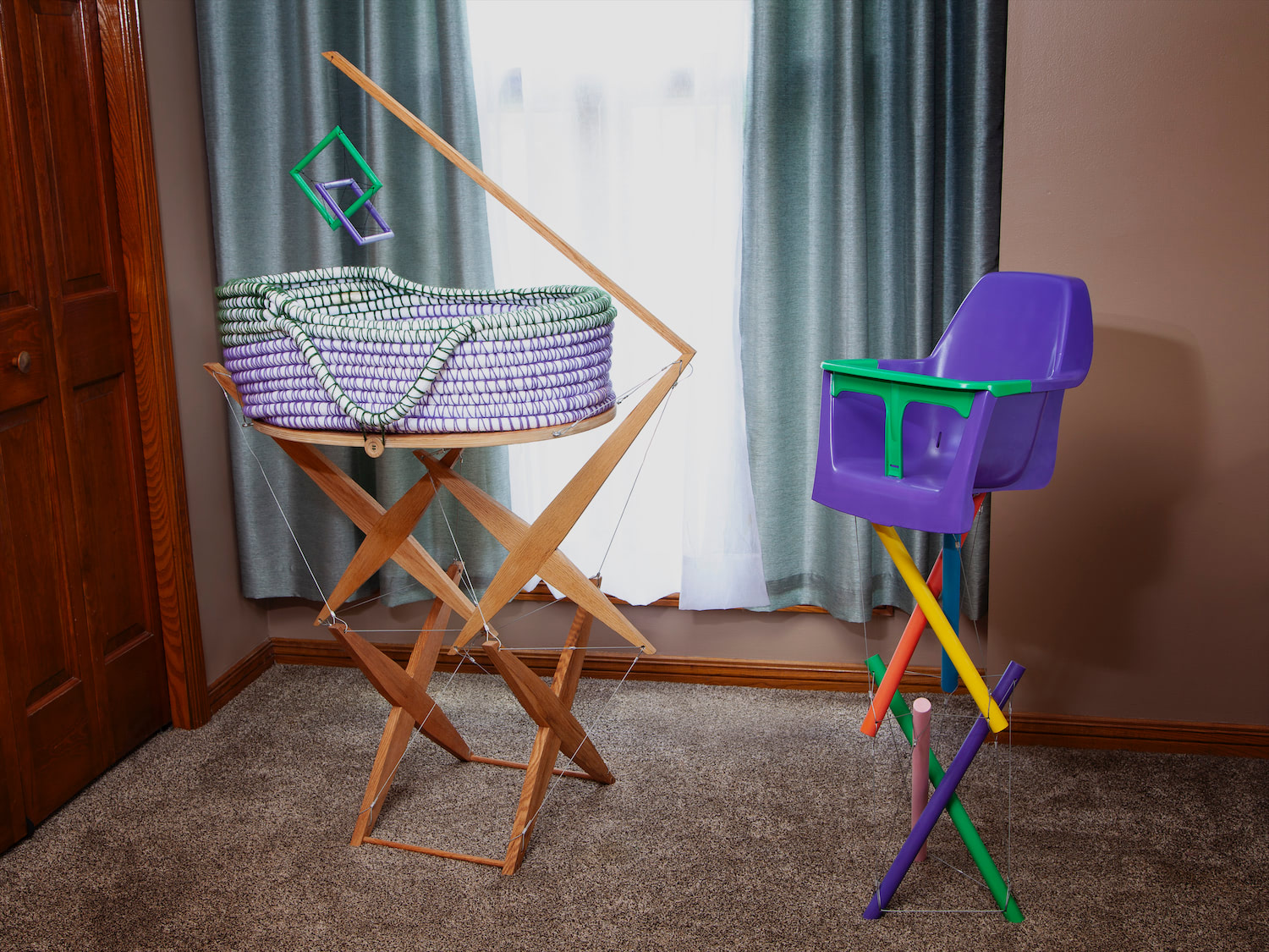 Tensegrity bassinet on a wood structure with a hanging tensegrity mobile and hand crocheted basket. Tensegrity high chair with six painted legs, three of which are completely suspended. Side by side in a bedroom.